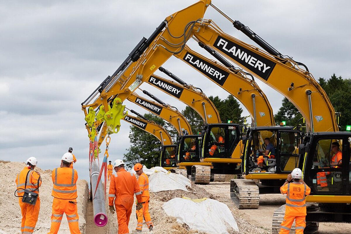 Crew placing large pipe in an excavated trench during field work