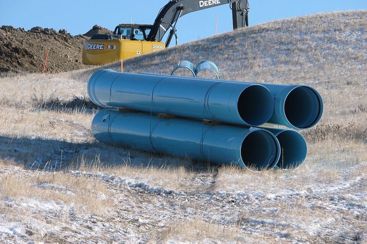 Large pipe sections staged beside excavation equipment for line repair work